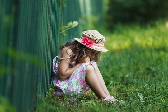 Sad little girl sitting on grass