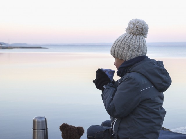 Child sitting on a pier and drinking tea on a cold evening